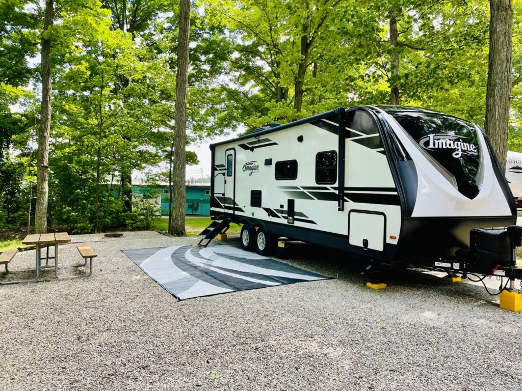 Imagine black and white travel trailer with mat and picnic table in trees