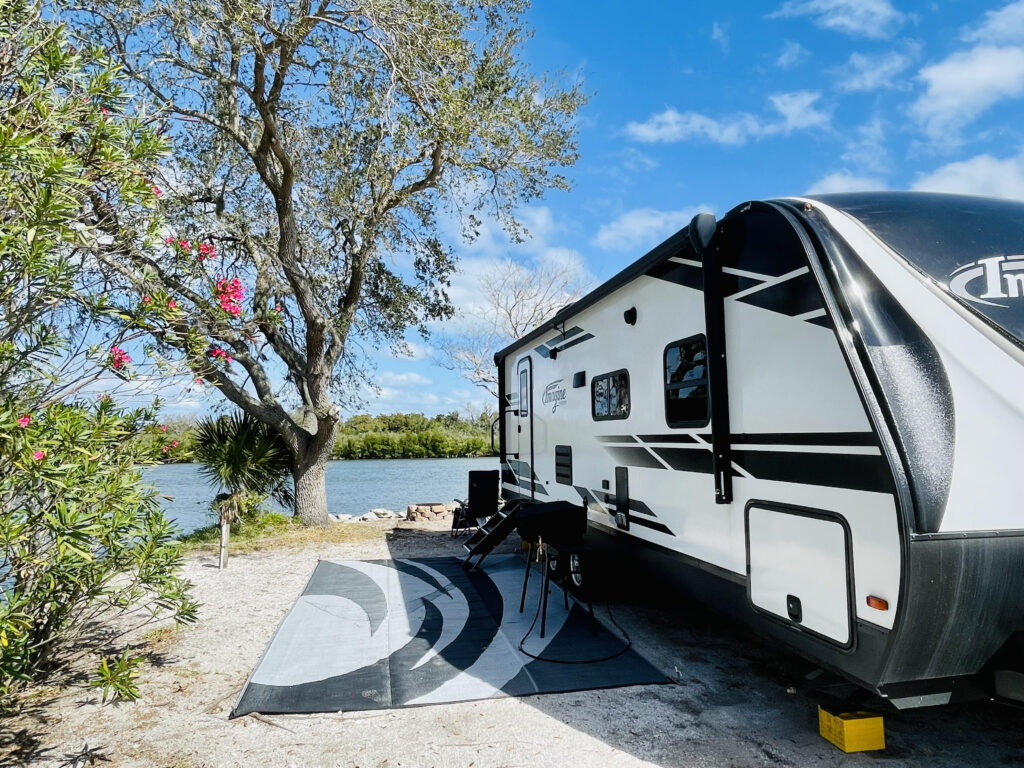 View of the side of black and white RV with river and colorful tree in background