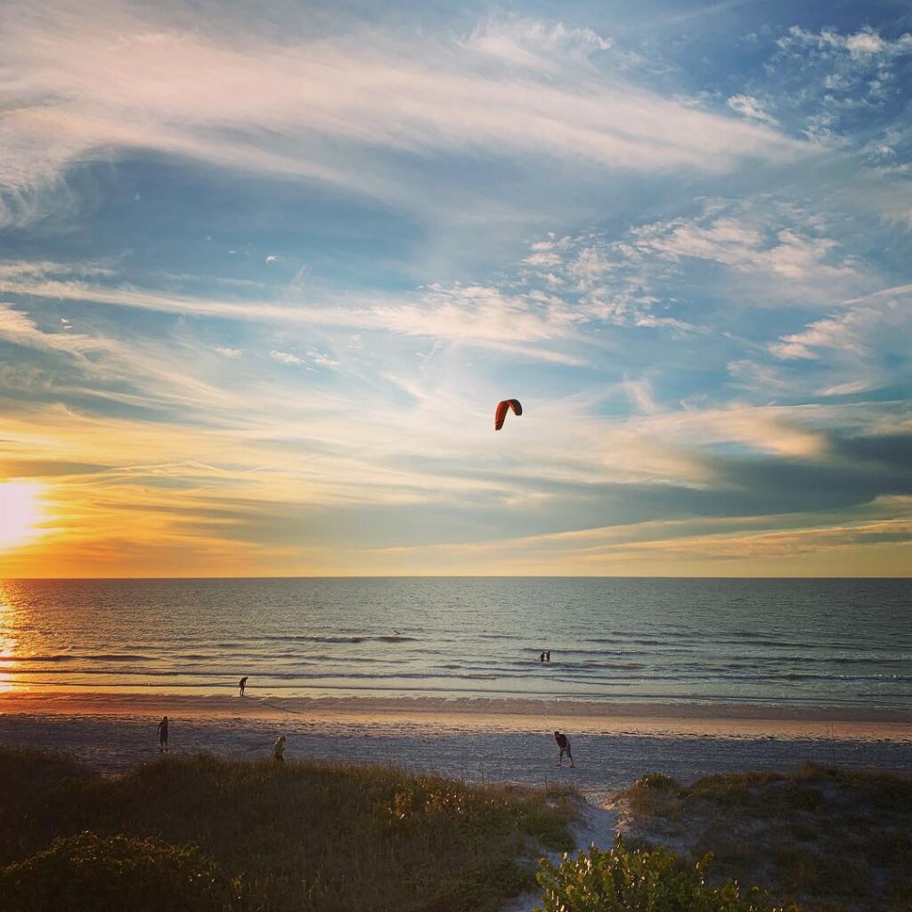 Orange sunset with kite in blue sky and clouds with beach and ocean