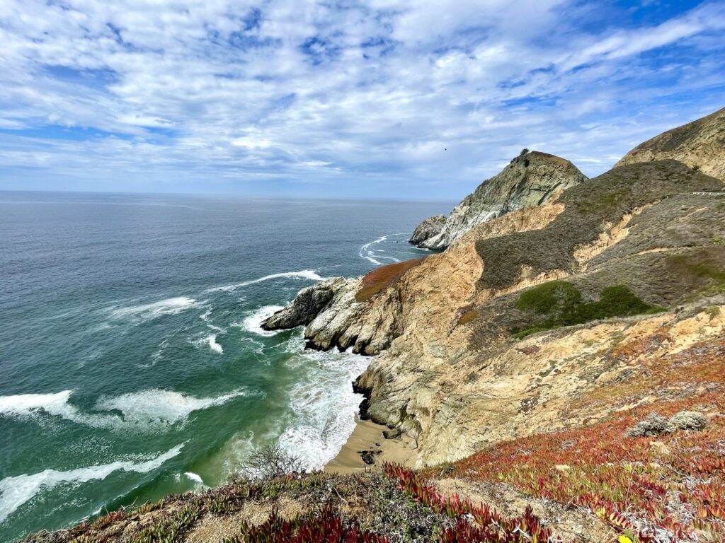 Clouds in a blue sky with rocky cliffs at the edge of the green Pacific ocean