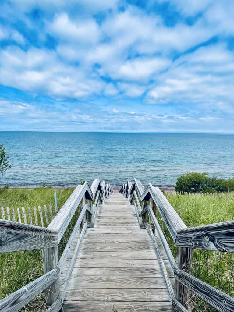 Board walk stairs lead to rocky beach and the blue lake waters with puffy white clouds in blue sky