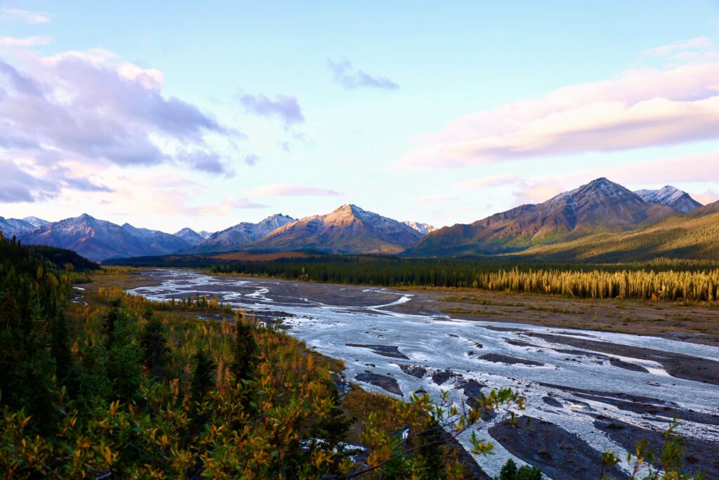 Sunlight hitting mountain peaks with a stream running all different ways and yellow, red, and green foliage