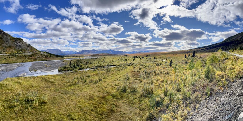 Landscape of blue cloudy skies, a stream, mountains in background,