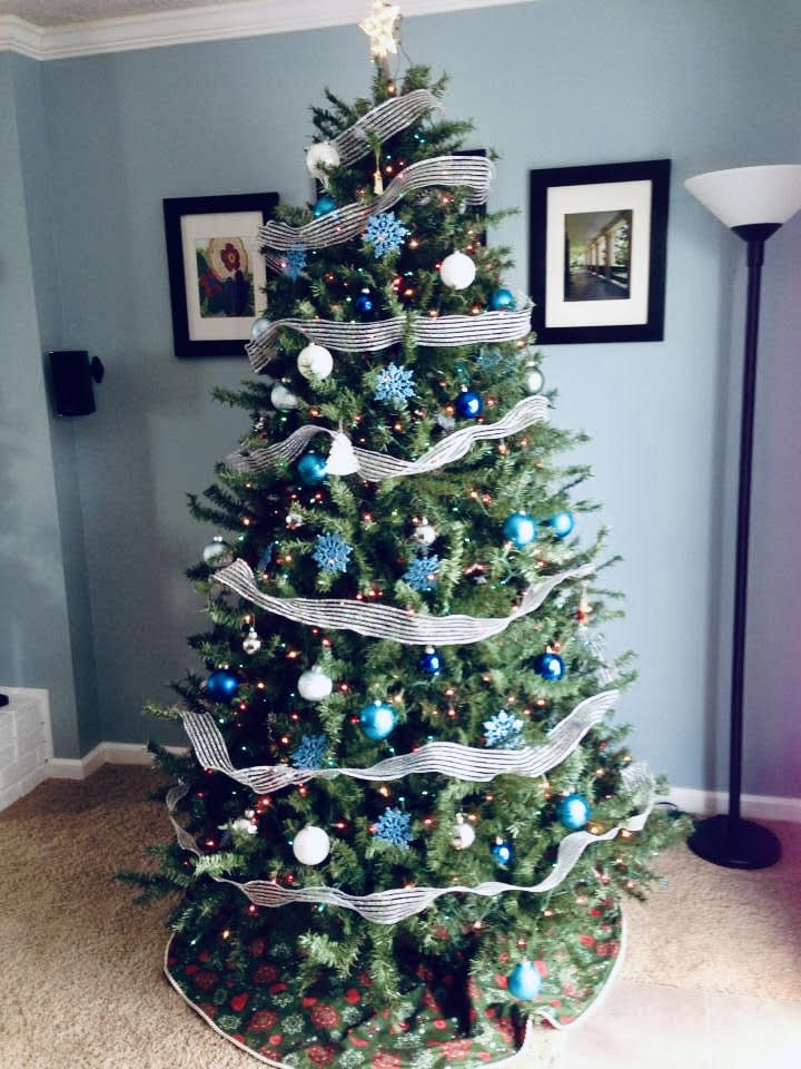 Christmas tree in living room with silver and blue ornaments against a gray wall