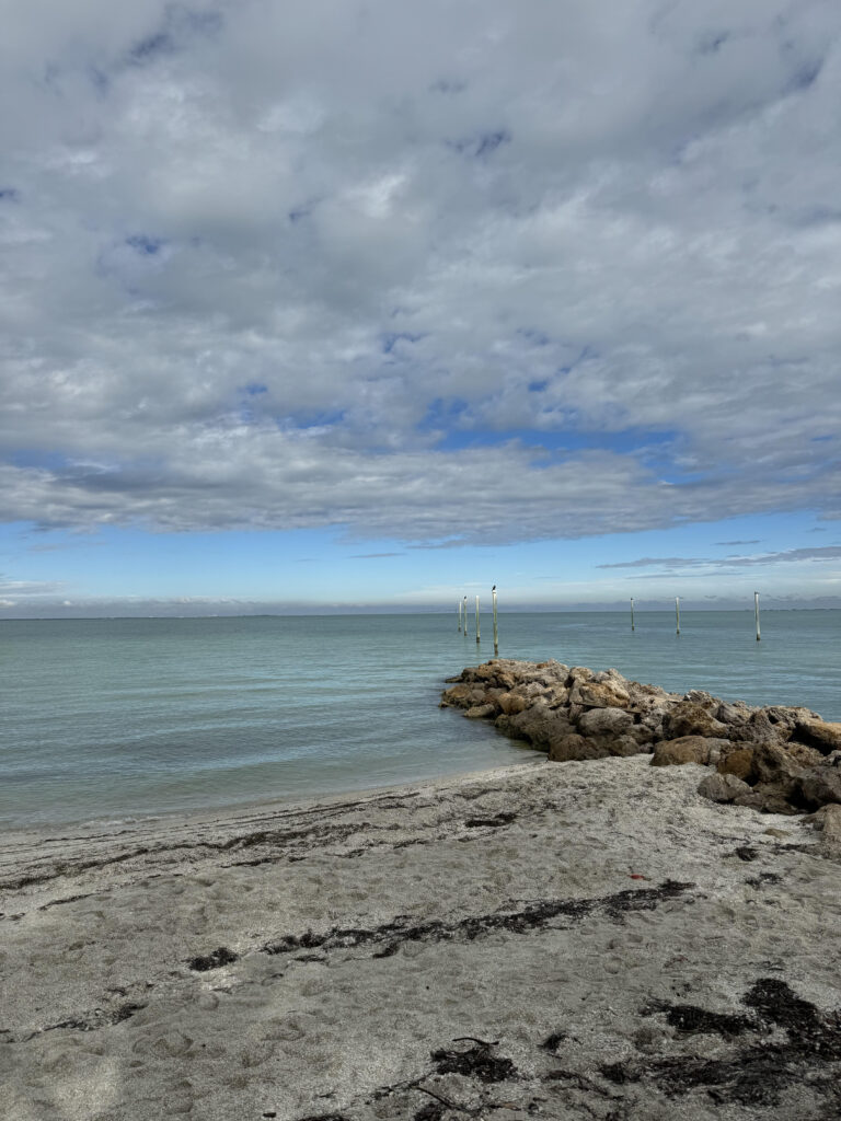 View of sandy beach with rock jetty into water with cloudy blue sky