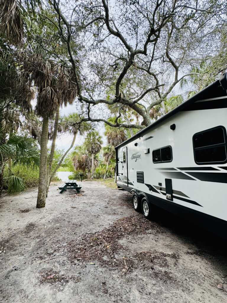 White and Black rv in sandy tree covered area with blue sky