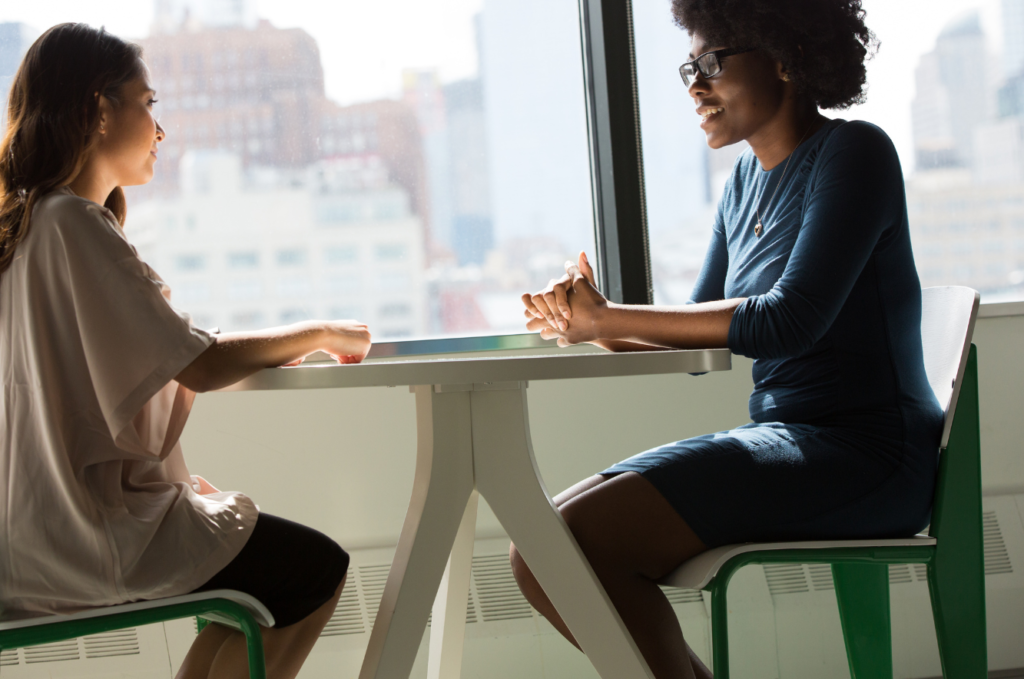Two people sitting at a table having a conversation with a window in the background