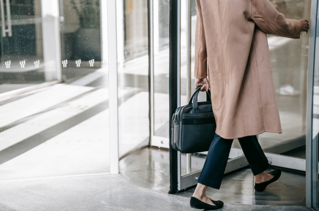 Shot of a person with a briefcase in a beige coat and nice shoes walking out a revolving door to leave