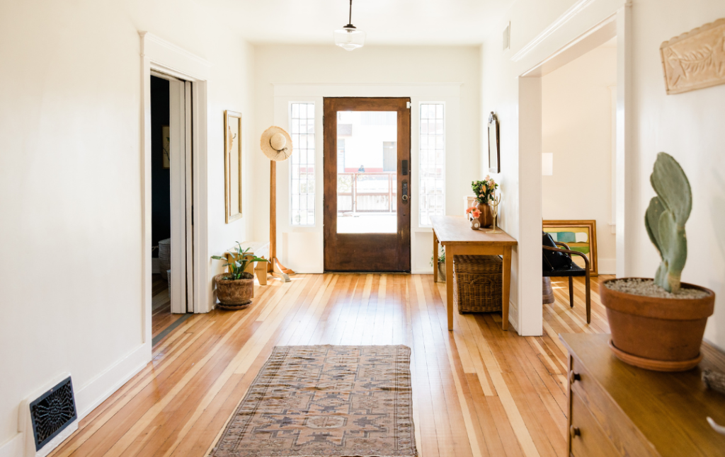 Home entry way with light streaming through door with hard wood floors, a rug and hall way tables